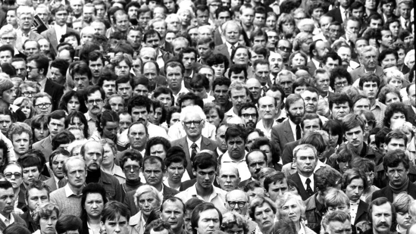 Zdjęcie przedstawia tłum ludzi. Widoczne są ich twarze. Zdjęcie jest czarno-białe.