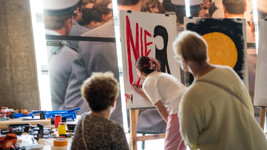 Seniorzy na wystawie stałej ECS, oglądają jak artystka maluje obraz